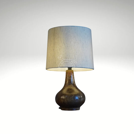 A rustic ceramic table lamp with a dark brown teardrop base and a light beige drum shade