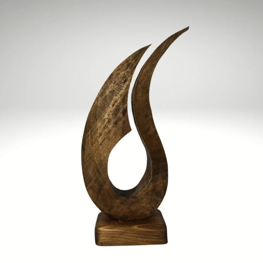 A contemporary abstract wooden sculpture shaped like a stylized, flowing flame with two tapering upward curves, mounted on a solid rectangular wooden base.
