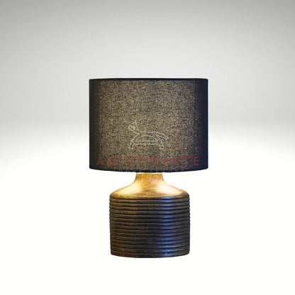 A modern table lamp featuring a dark, ribbed cylindrical wooden base paired with a sleek black drum fabric shade.