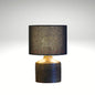 A modern table lamp featuring a dark, ribbed cylindrical wooden base paired with a sleek black drum fabric shade.
