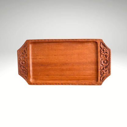 A rectangular wooden serving tray with detailed floral carvings on both handles