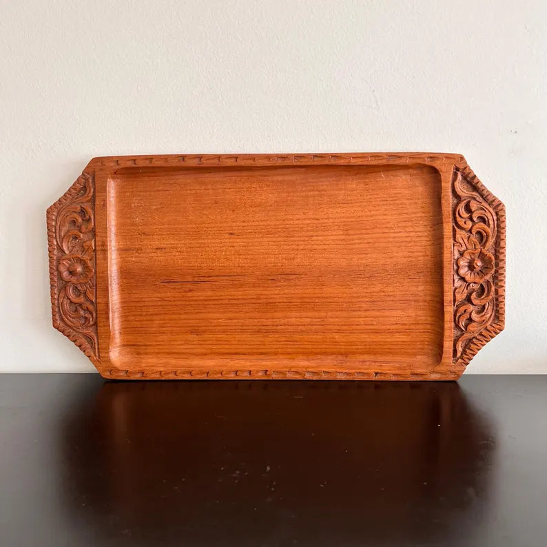 A rectangular wooden serving tray with detailed floral carvings on both handles