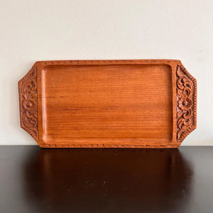 A rectangular wooden serving tray with detailed floral carvings on both handles