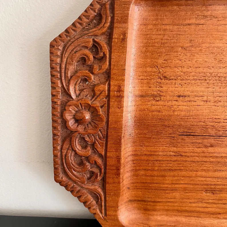 A rectangular wooden serving tray with detailed floral carvings on both handles