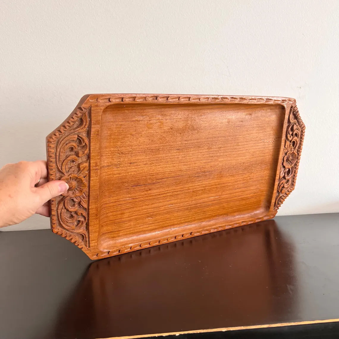 A rectangular wooden serving tray with detailed floral carvings on both handles