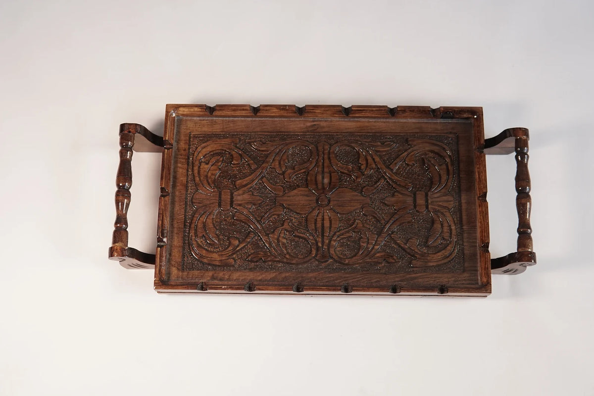 A rectangular wooden serving tray with detailed floral carvings on both handles and a smooth natural grain finish.