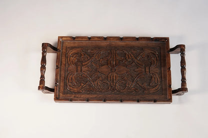A rectangular wooden serving tray with detailed floral carvings on both handles and a smooth natural grain finish.