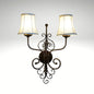 A rustic double-light wall sconce with a decorative dark metal scrollwork frame and two glowing cream fabric lampshades.