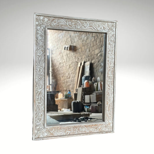A rectangular wall mirror with a wide, ornate wooden frame featuring detailed floral and vine carvings with a distressed white-wash finish.
