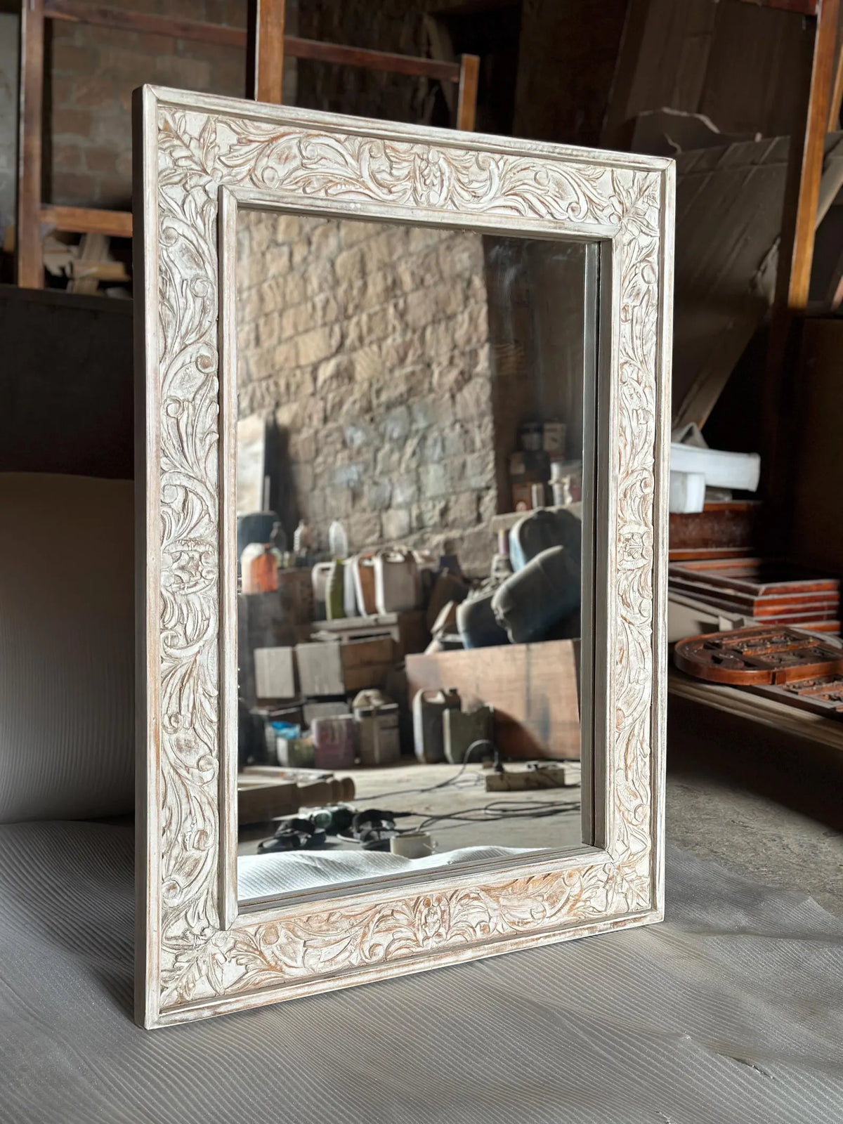 A rectangular wall mirror with a wide, ornate wooden frame featuring detailed floral and vine carvings with a distressed white-wash finish.