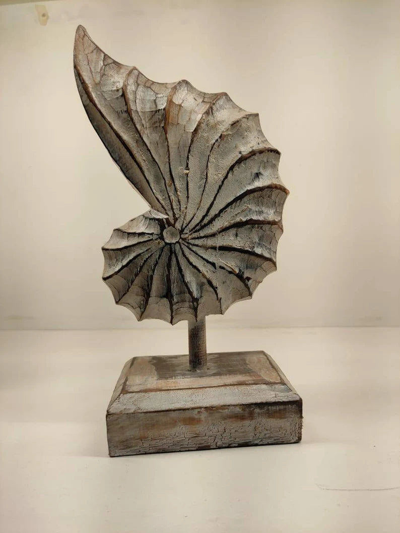 A hand-carved wooden nautilus shell sculpture with a distressed white finish.