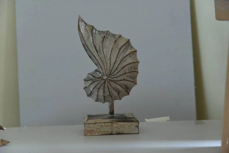 A hand-carved wooden nautilus shell sculpture with a distressed white finish.