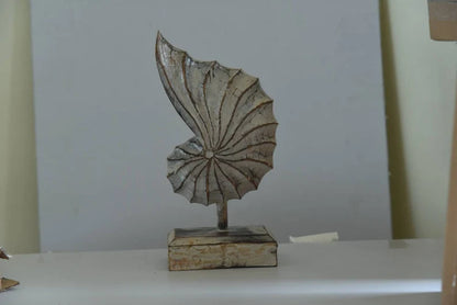 A hand-carved wooden nautilus shell sculpture with a distressed white finish.