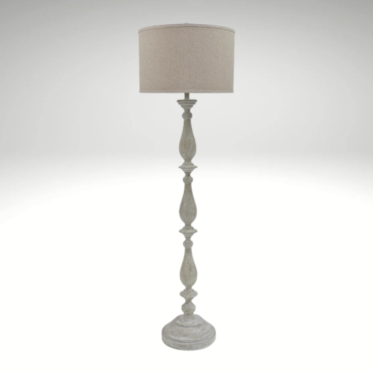 A distressed antique white floor lamp with a carved wooden-style base and a neutral beige fabric drum shade.