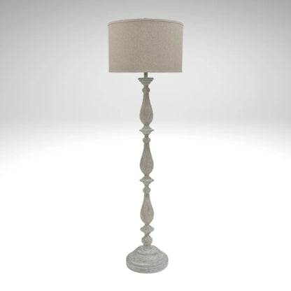 A distressed antique white floor lamp with a carved wooden-style base and a neutral beige fabric drum shade.