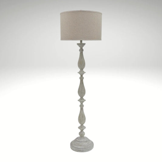 A distressed antique white floor lamp with a carved wooden-style base and a neutral beige fabric drum shade.
