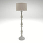 A distressed antique white floor lamp with a carved wooden-style base and a neutral beige fabric drum shade.