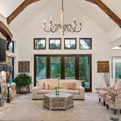 An elegant antique-style metal chandelier featuring sweeping curved arms, candle-style bulbs, and decorative crystal pendants illuminated by warm yellow light.