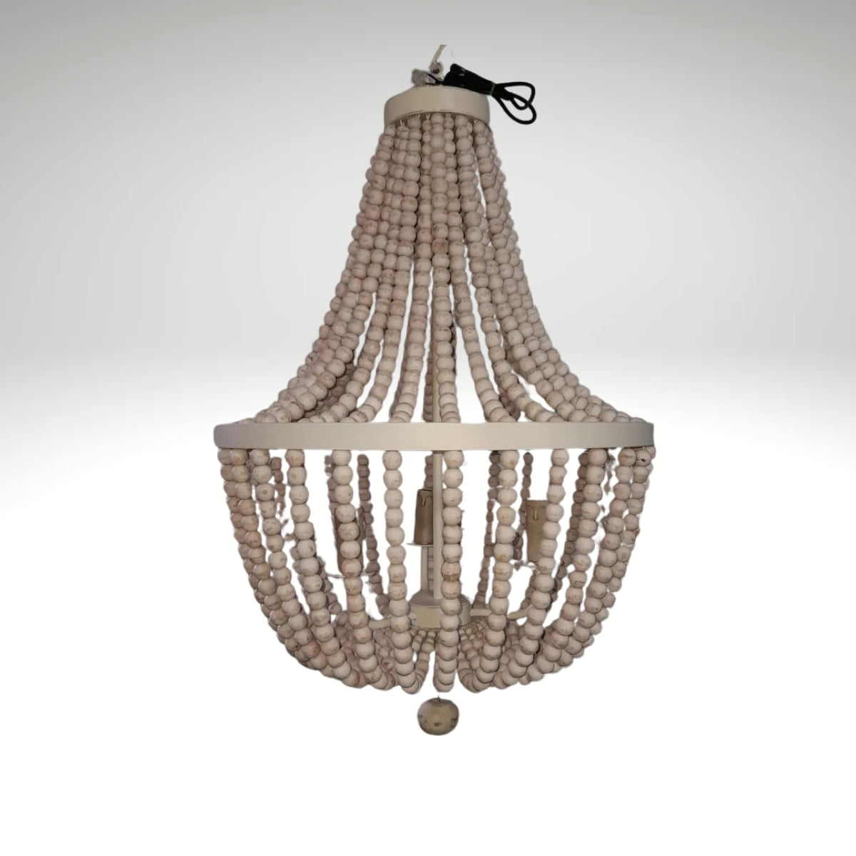 A rustic boho chandelier made of cascading strands of white wooden beads hung from a circular metal frame.
