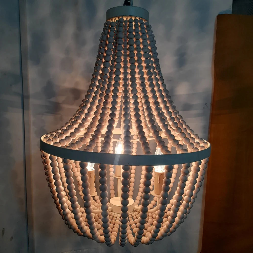A rustic boho chandelier made of cascading strands of white wooden beads hung from a circular metal frame.