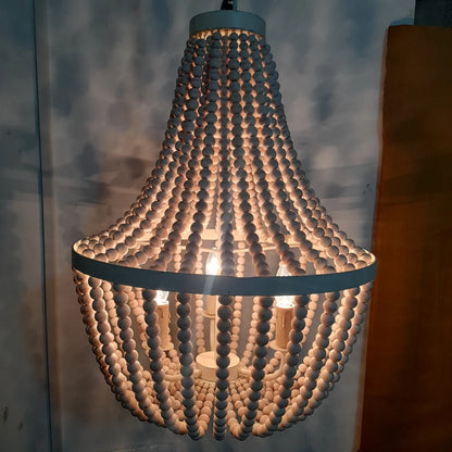 A rustic boho chandelier made of cascading strands of white wooden beads hung from a circular metal frame.
