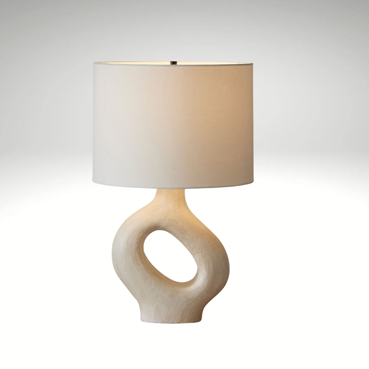 An off-white textured ceramic lamp featuring a hollow doughnut-shaped base and a classic white lampshade.