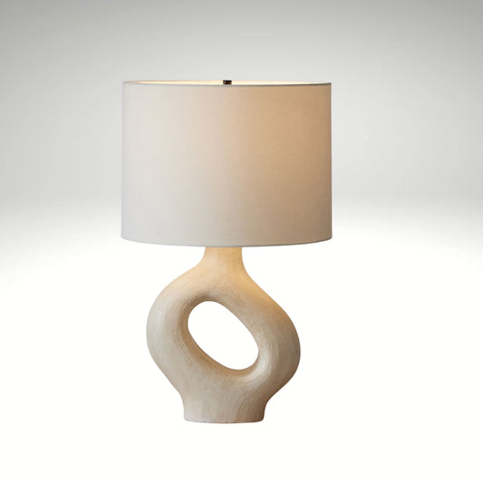 An off-white textured ceramic lamp featuring a hollow doughnut-shaped base and a classic white lampshade.