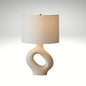 An off-white textured ceramic lamp featuring a hollow doughnut-shaped base and a classic white lampshade.