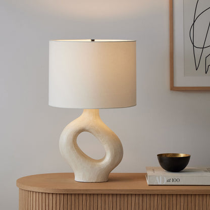 An off-white textured ceramic lamp featuring a hollow doughnut-shaped base and a classic white lampshade.