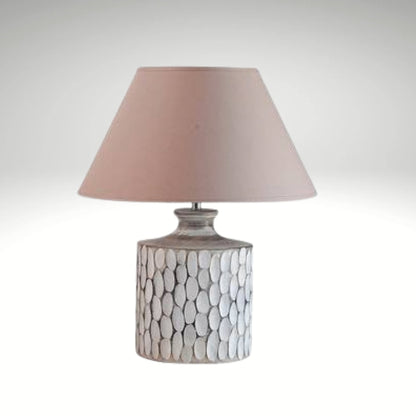 A rustic white ceramic table lamp featuring a textured, carved oval pattern on a cylindrical base with a beige fabric shade.