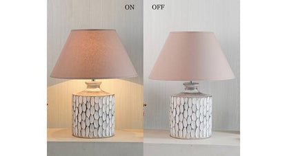 A rustic white ceramic table lamp featuring a textured, carved oval pattern on a cylindrical base with a beige fabric shade.