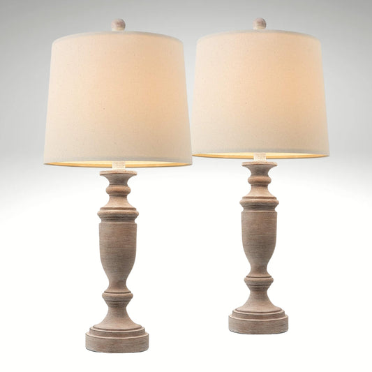 A rustic table lamp featuring a distressed faux wood baluster base and a classic cream fabric drum shade.