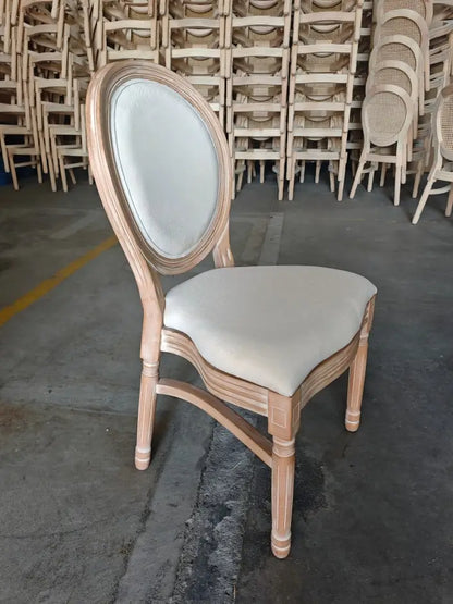 A rustic French country dining chair featuring an oval upholstered backrest and a weathered wooden frame.