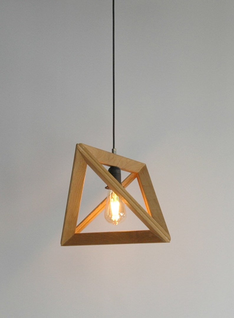 A minimalist pyramid-shaped wooden hanging lamp with a warm glowing light bulb.
