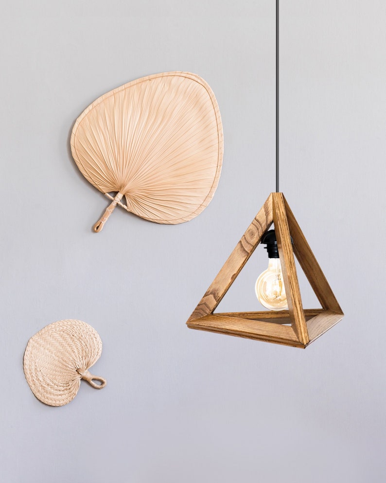 A minimalist pyramid-shaped wooden hanging lamp with a warm glowing light bulb.