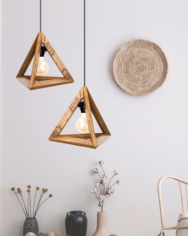 A minimalist pyramid-shaped wooden hanging lamp with a warm glowing light bulb.