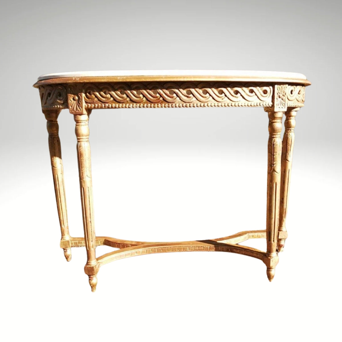 Giltwood console table with a marble top and fluted legs, placed outdoors on a stone patio.