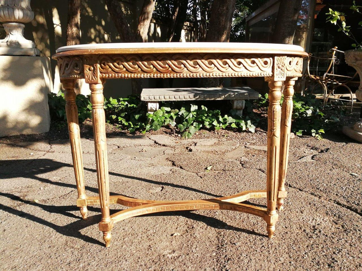 Giltwood console table with a marble top and fluted legs, placed outdoors on a stone patio.