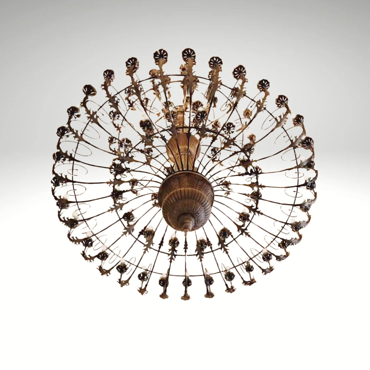 An antique bronze finish round chandelier featuring detailed leaf patterns, multiple small light bulbs, and a radial cage design.