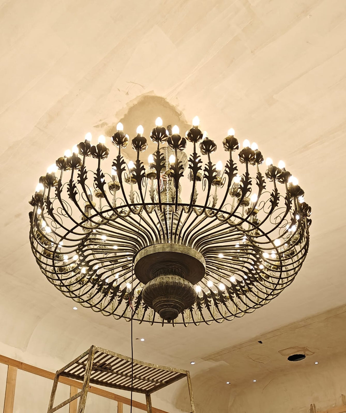 An antique bronze finish round chandelier featuring detailed leaf patterns, multiple small light bulbs, and a radial cage design.