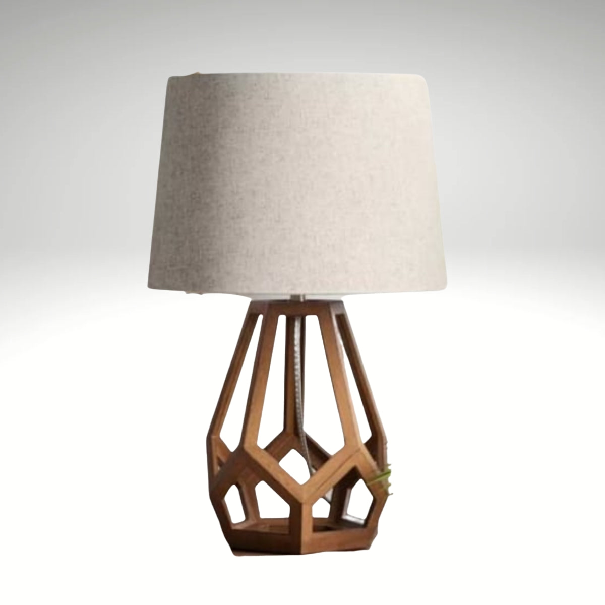 A modern table lamp featuring a brown geometric hollow wood base and a light beige fabric drum shade.