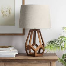 A modern table lamp featuring a brown geometric hollow wood base and a light beige fabric drum shade.