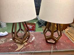 A modern table lamp featuring a brown geometric hollow wood base and a light beige fabric drum shade.