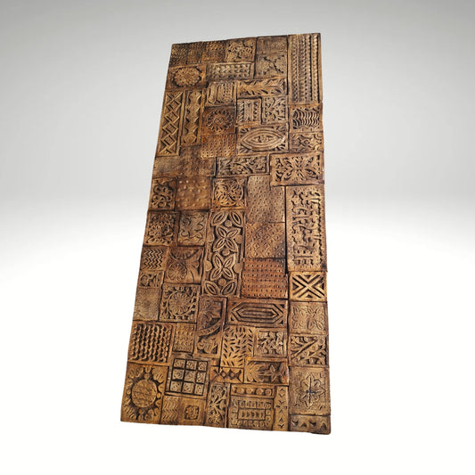 Antique-style carved wooden blocks arranged in a mosaic pattern to form a textured decorative wall panel with a rich brown finish.