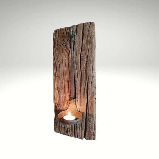 Vintage rustic wall lamp made of a textured reclaimed wood board with a hanging old iron ladle holding a lit tea light candle.