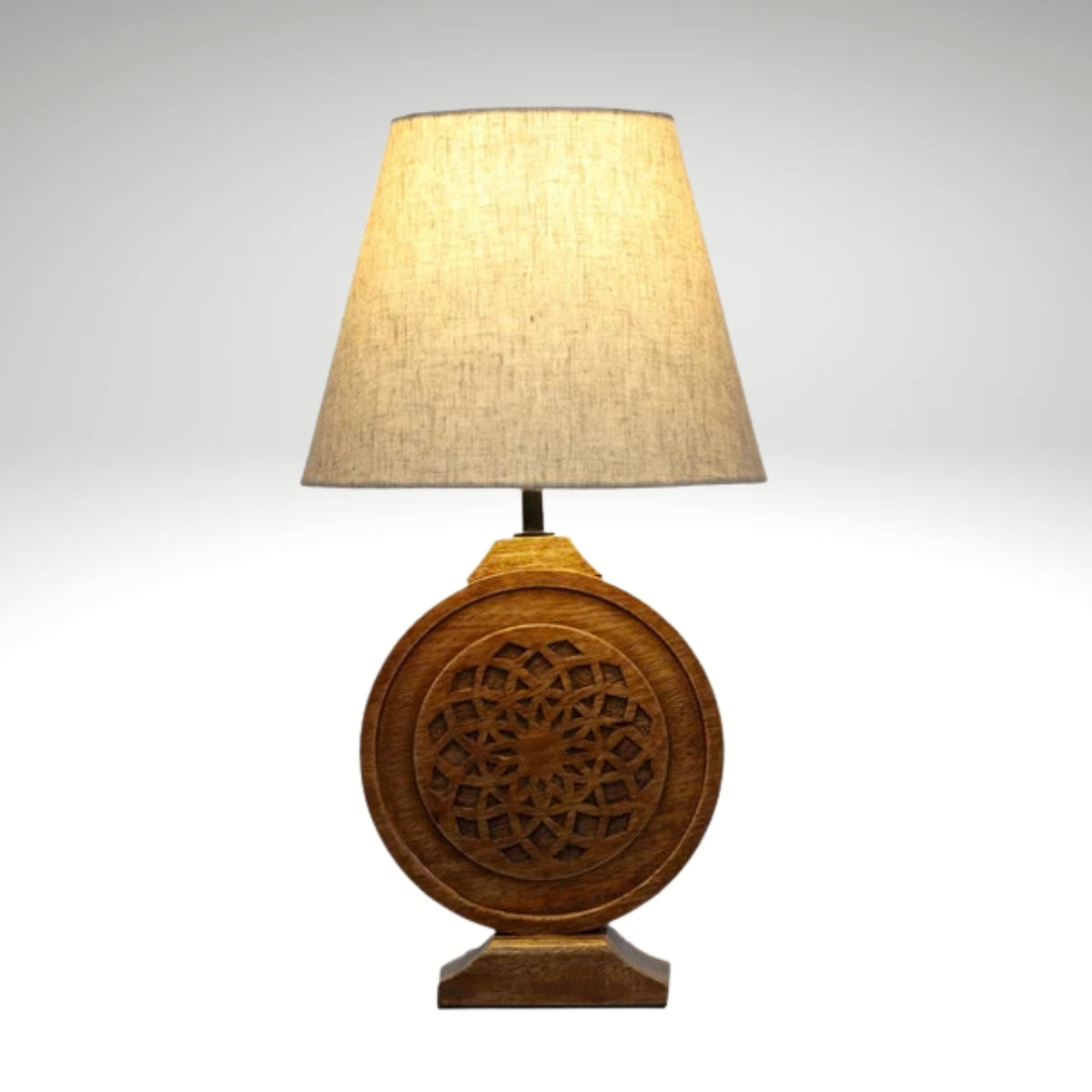 Bohemian-style table lamp with a round, carved wood mandala base and a neutral fabric lampshade