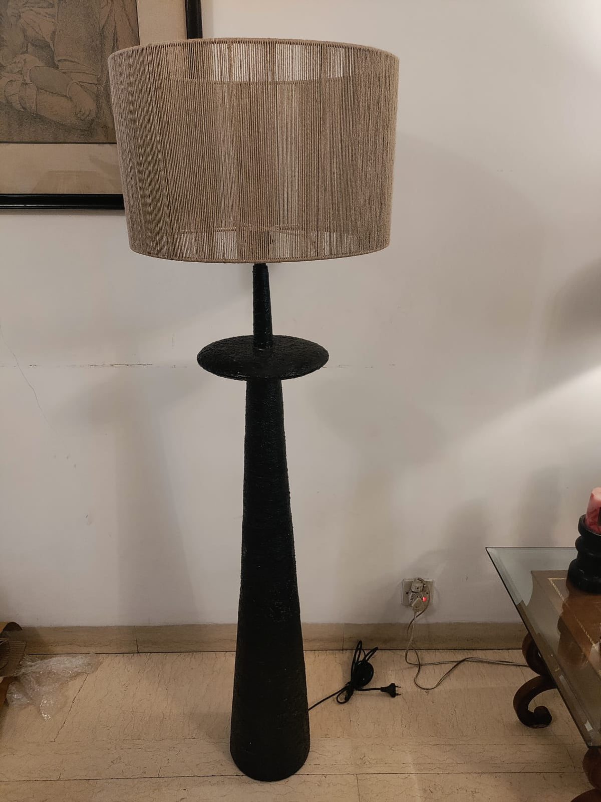A minimalist sculptural floor lamp showcasing a matte black textured column base paired with a beige string-detailed lampshade.