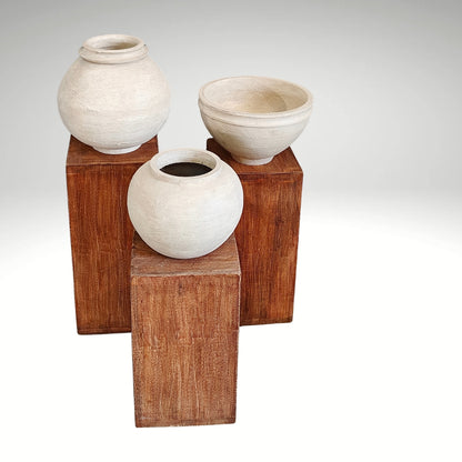 Minimalist wooden display risers holding handcrafted white clay vases in a multi-level arrangement.