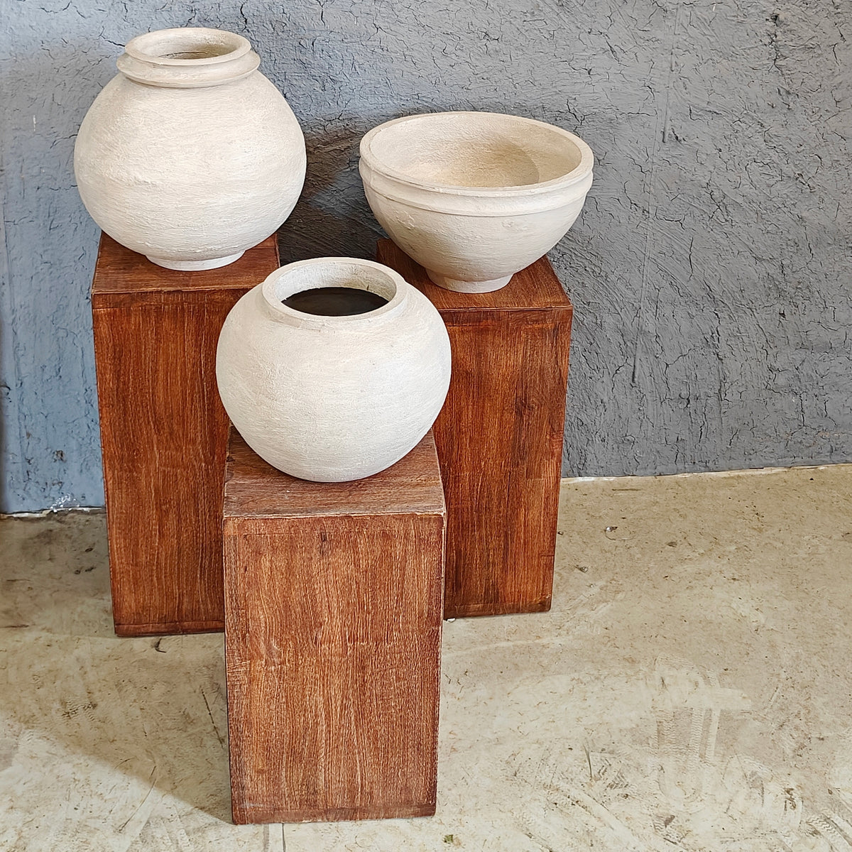 Minimalist wooden display risers holding handcrafted white clay vases in a multi-level arrangement.