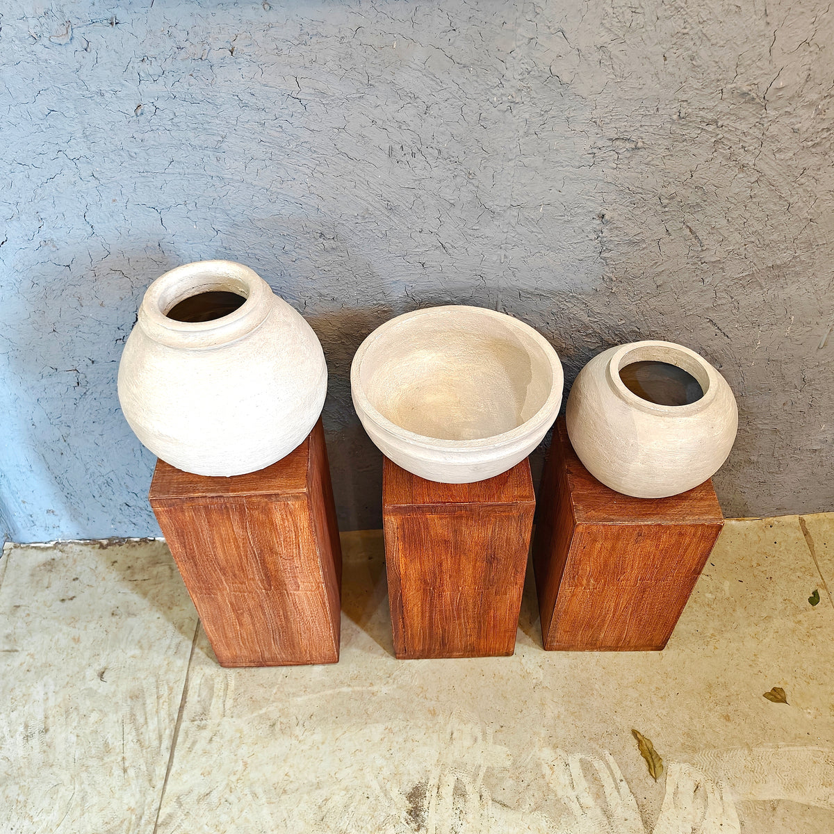 Minimalist wooden display risers holding handcrafted white clay vases in a multi-level arrangement.